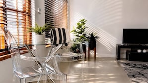A modern living room with clear chairs, a striped towel, potted plants, and a TV stand.