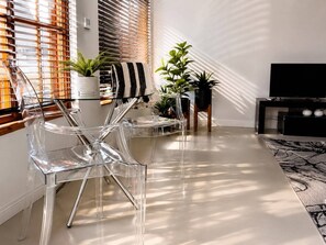 A modern living room with clear chairs, a striped towel, potted plants, and a TV stand.