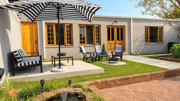 A patio with outdoor furniture, a striped umbrella, and a small water feature.