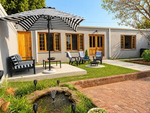 A patio with outdoor furniture, a striped umbrella, and a small water feature.