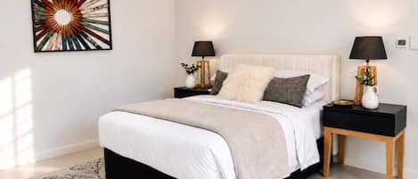 Un dormitorio con una cama grande, dos mesitas de noche, un adorno en la pared y un tapete estampado.