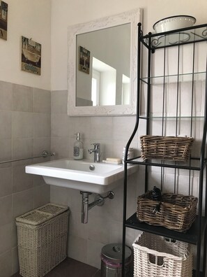 A bathroom with a white sink, a mirror, and wicker baskets on shelves. - NOI DUE Guesthouse (Fubine)