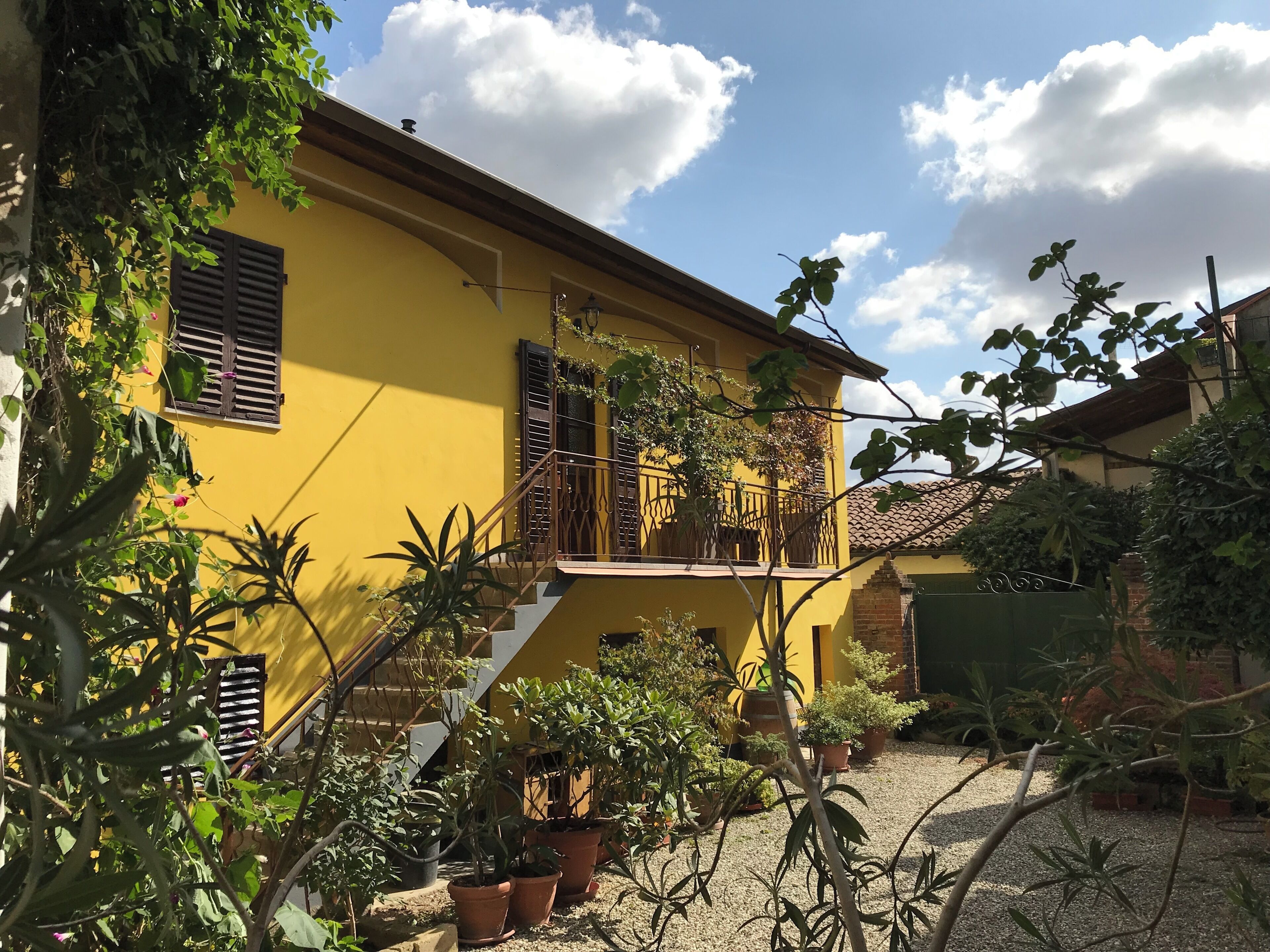 Ein gelbes Gebäude mit Balkon, Blumentöpfen und einem Kieshof.