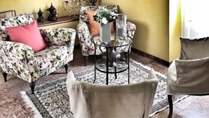 A room with a floral-patterned armchair, a round table with a vase, and a patterned rug. - NOI DUE Guesthouse (Fubine)