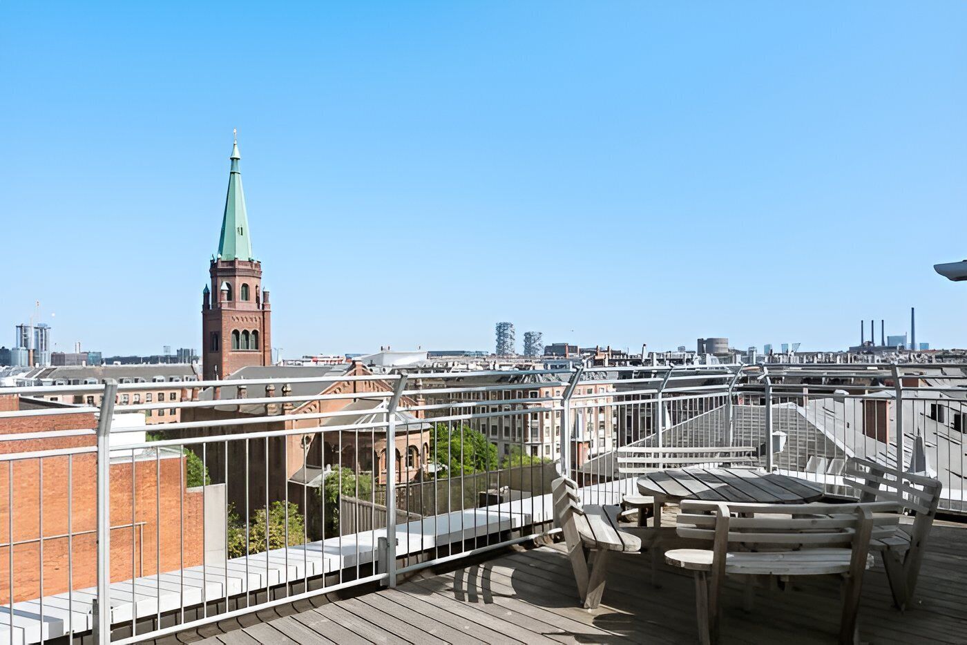 A rooftop terrace with a view of a city skyline, including a prominent tower with a green spire.