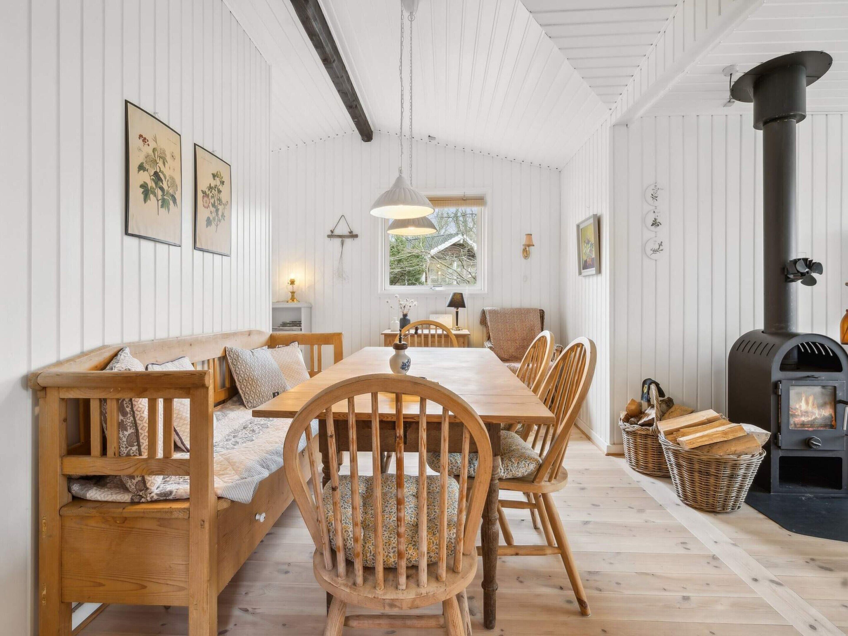 A cozy room with a wooden bench, a dining table, chairs, a fireplace, and framed botanical prints on the wall.