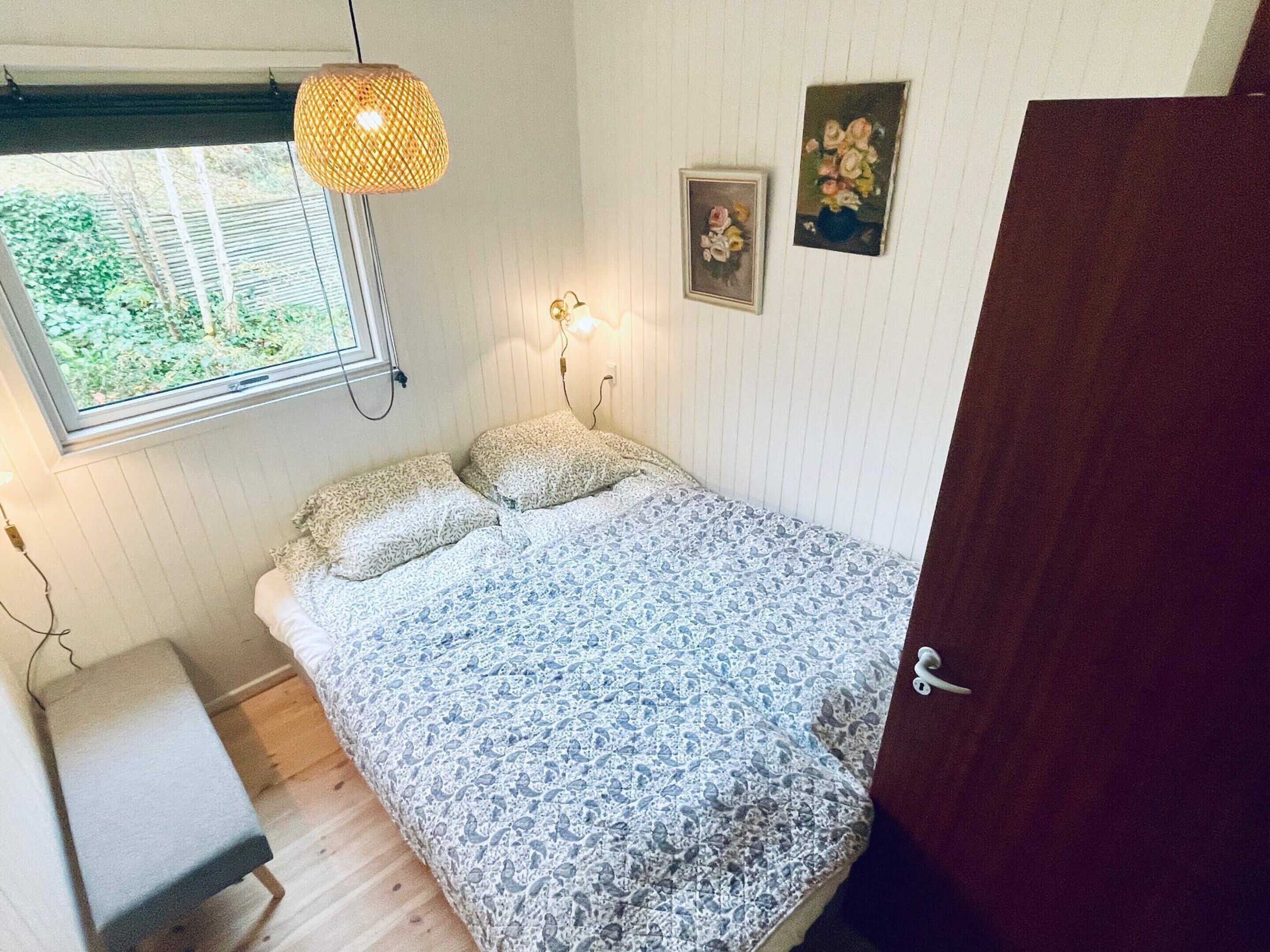 Une chambre à coucher avec un lit, une fenêtre, une lampe fixée au mur et une porte.