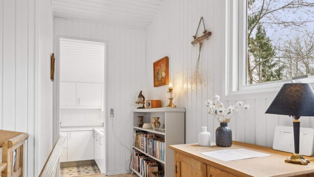 A room with a wooden desk, a bookshelf, a window with a view of trees, and a door leading to another room. - 5 Star Holiday Home in Glesborg (Glesborg)