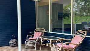 A covered outdoor seating area with wicker furniture and a table, a metal lantern, and a view of greenery through a window. - 5 Star Holiday Home in Glesborg (Glesborg)