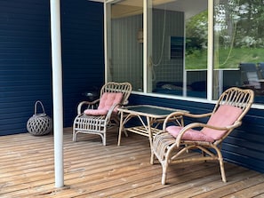 A covered outdoor seating area with wicker furniture and a table, a metal lantern, and a view of greenery through a window. - 5 Star Holiday Home in Glesborg (Glesborg)
