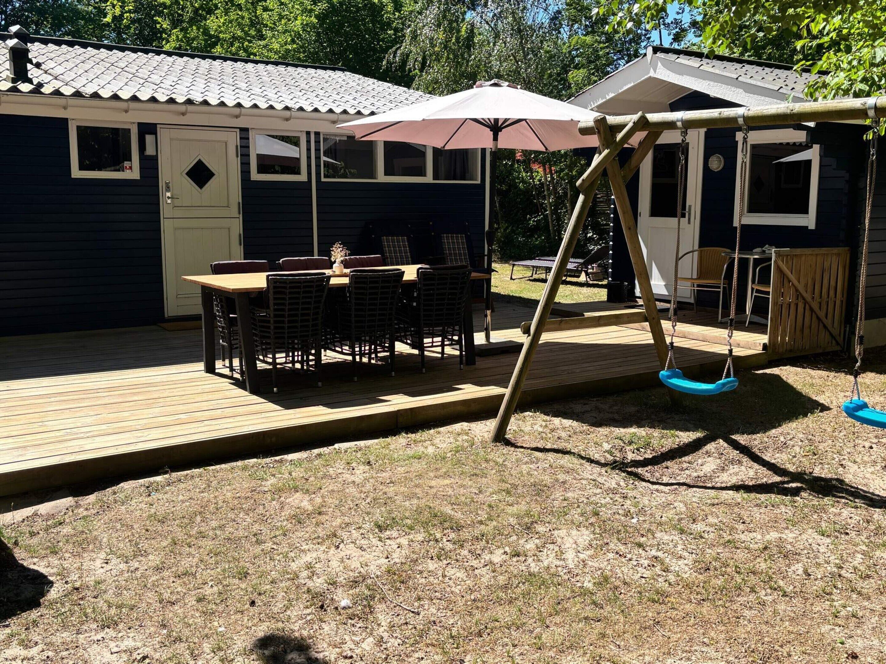 A wooden deck with a table and chairs, a swing set, and a covered area with an umbrella.