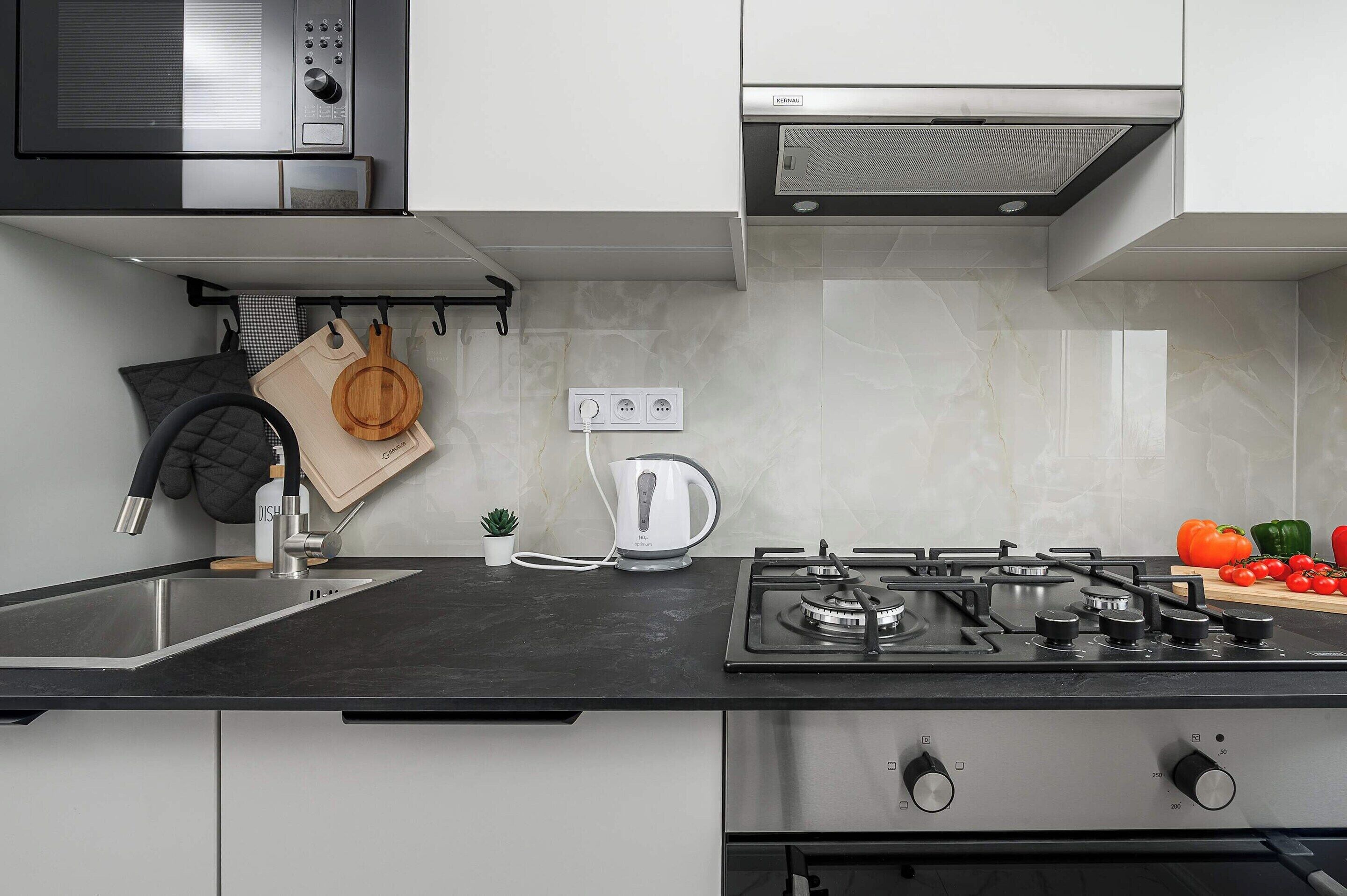 Een moderne keuken met een zwart aanrechtblad, roestvrijstalen apparatuur en diverse keukengerei.