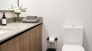 Ein modernes Badezimmer mit einem Holzwaschtisch, einer Toilette und einem Mülleimer.