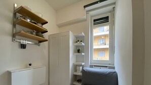 Ein kleiner Raum mit Bett, Einbauschränken, einem Kleiderschrank und einem Fenster mit Blick auf ein Gebäude.