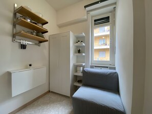 Ein kleiner Raum mit Bett, Einbauschränken, einem Kleiderschrank und einem Fenster mit Blick auf ein Gebäude.