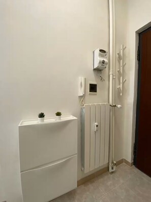 Ein Badezimmer mit weißem Heizkörper, Wandheizung, Handtuchhalter und einer kleinen Topfpflanze auf einem Regal.