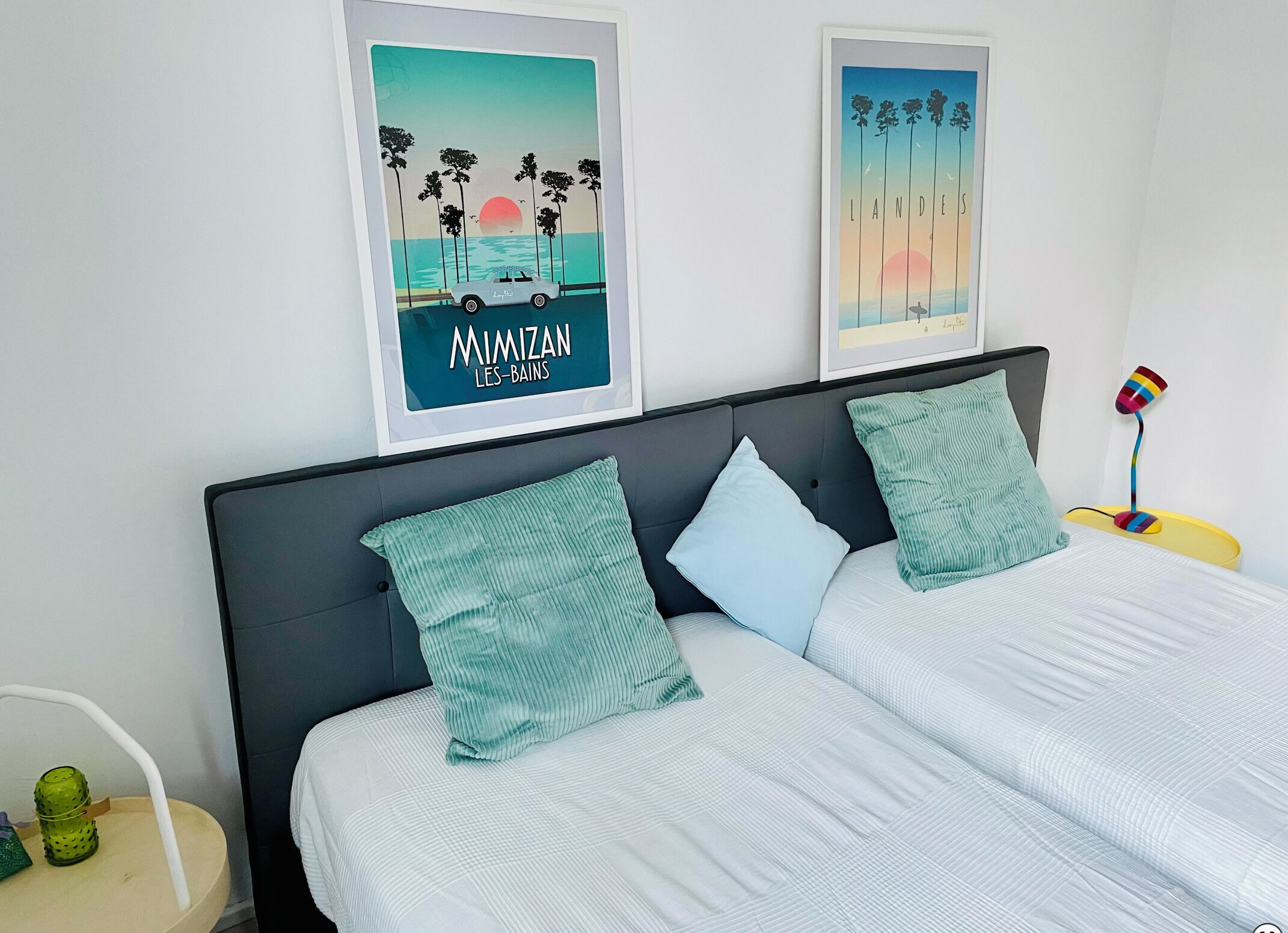 Un lit avec deux oreillers, une table de chevet avec une lampe et deux tableaux encadrés accrochés au mur.