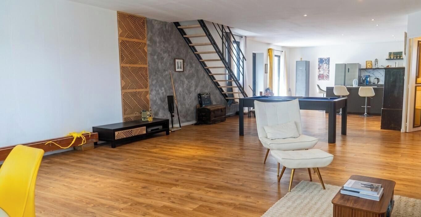 Ein geräumiger Wohnbereich mit Holzboden, einem weißen Sessel, einem Esstisch und einer Treppe.
