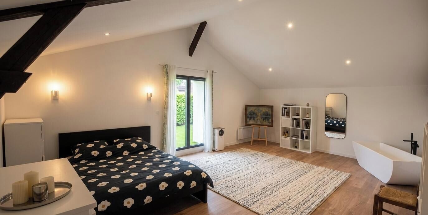 A bedroom with a bed, bedside table, lamp, and a view of the outdoors.