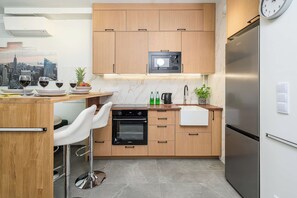 Eine moderne Küche mit Holzausbau, einer eingebauten Mikrowelle, einem Edelstahlkühlschrank und einer Bar mit einem weißen Stuhl.
