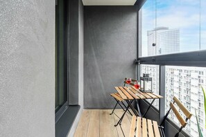 A balcony with a wooden table and chairs, a small lantern, and a view of a cityscape. - Lush Home With City Views (Warsaw)