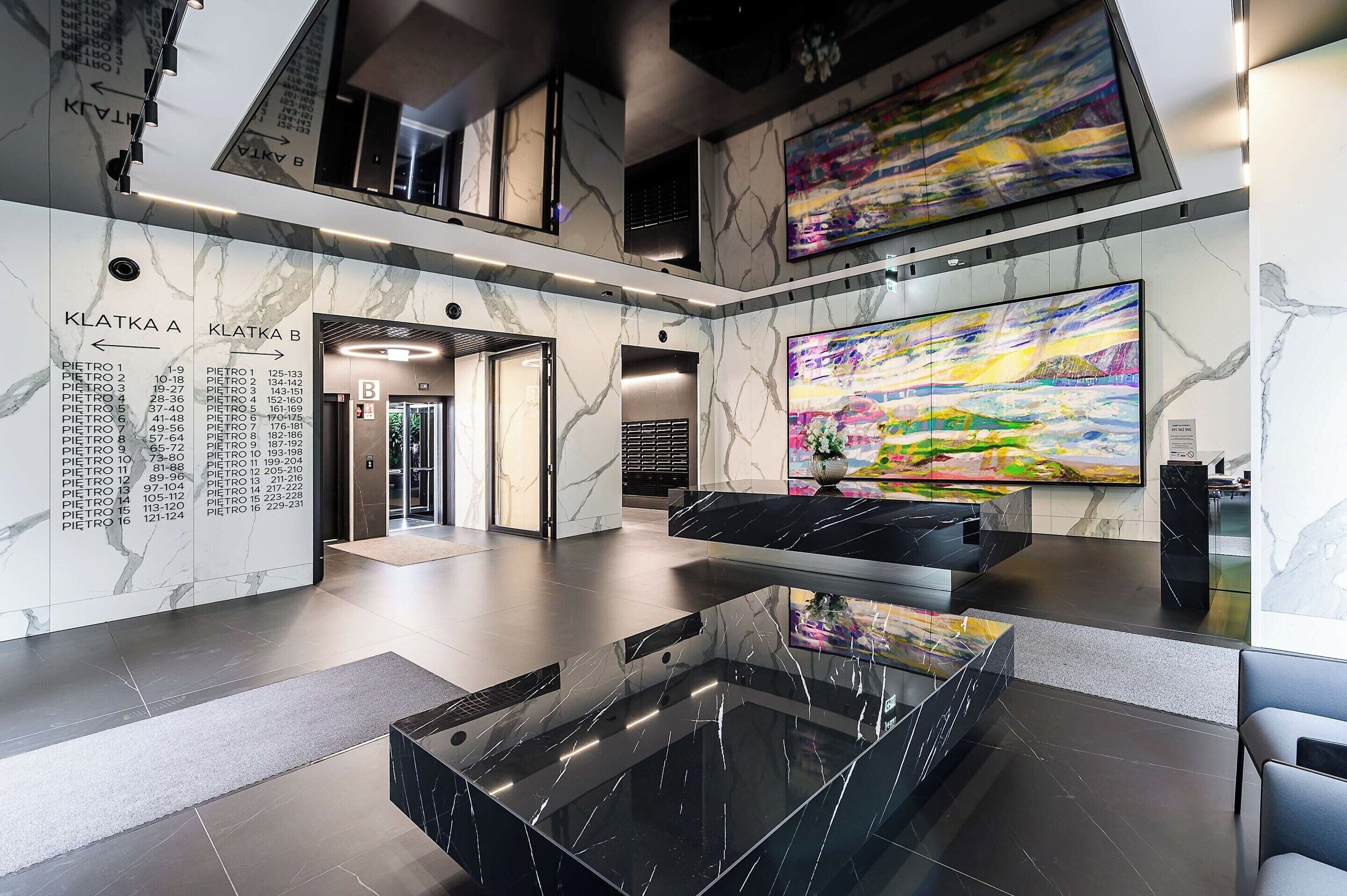 A modern lobby with a marble floor, a glass coffee table, and a large abstract painting.