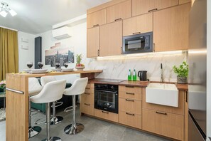 A modern kitchen with wooden cabinets, a built-in microwave, a stainless steel sink, and a bar area with two white bar stools. - Lush Home With City Views (Warsaw)