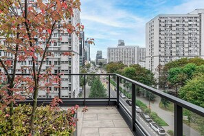 A high-rise building with multiple floors, a balcony with a glass railing, and a view of a city street with cars. - Lush Home With City Views (Warsaw)