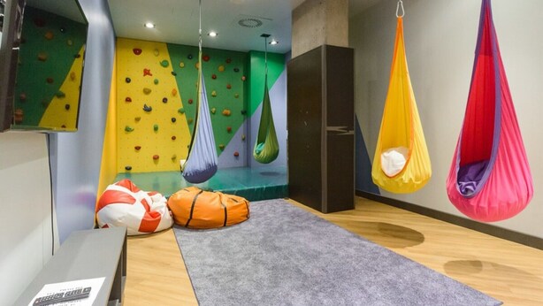 A room with a climbing wall, hanging hammocks, a yoga mat, and a desk with a remote control. - City Apartment With Balcony (Warsaw)