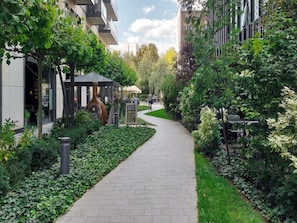 A paved pathway flanked by lush greenery and modern buildings. - City Apartment With Balcony (Warsaw)