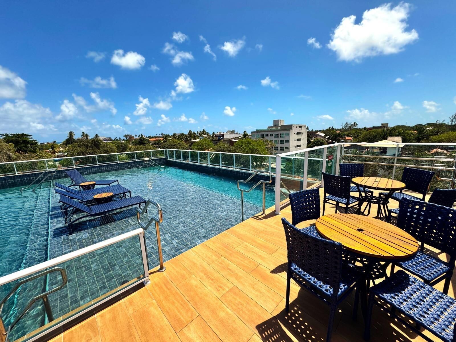 A rooftop pool area with lounge chairs and tables, surrounded by a glass railing.