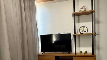 Quarto moderno com televisão de tela plana em um suporte de madeira, um sofá e uma prateleira fixada na parede com objetos decorativos.