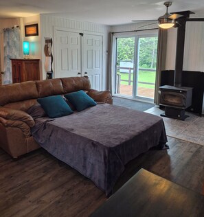 Quarto aconchegante com sofá de couro marrom, colcha roxa, piso de madeira, lareira e porta de vidro deslizante para o exterior.