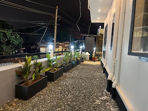 A rooftop terrace with potted plants, a gravel pathway, and a building facade with windows and pipes.