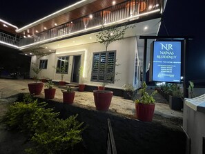 A modern building with a sign for Natinas Residency, featuring a balcony with railings and potted plants.