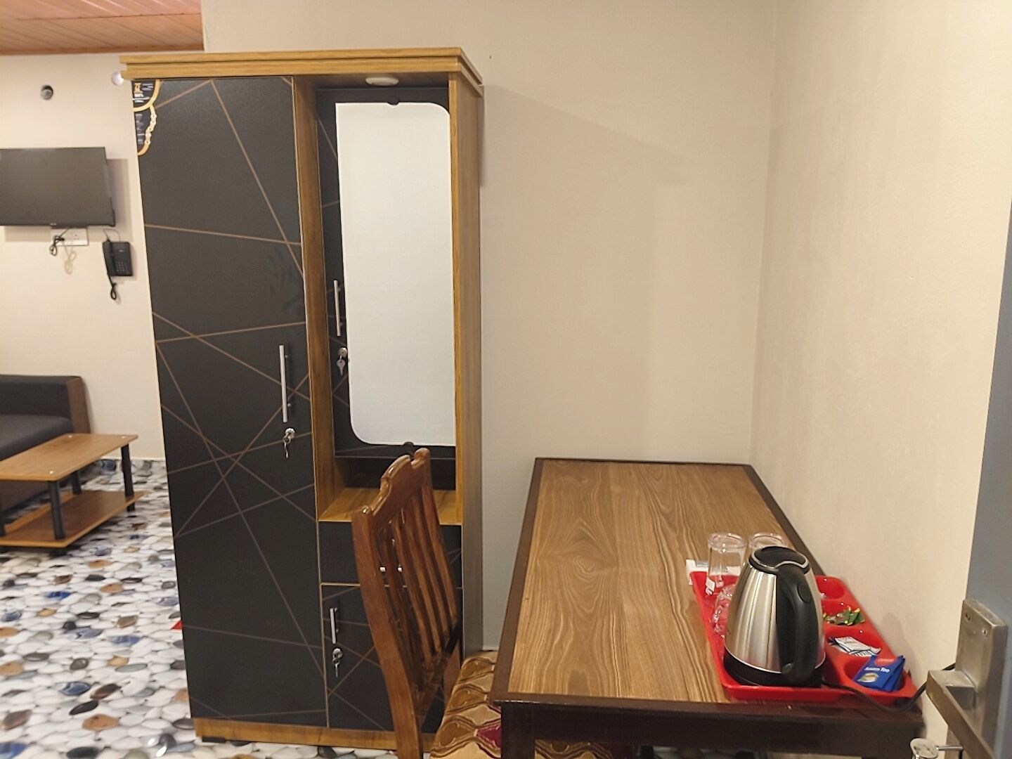 Una habitación compacta con una mesa de madera para comer, una silla, una pequeña área de kitchenette y un televisor montado en la pared.