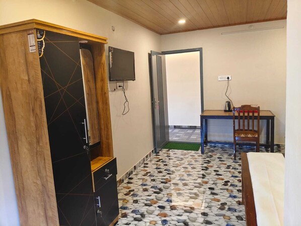 A hotel room with a wardrobe, a television mounted on the wall, a small table with a chair, and a pebble-patterned floor.