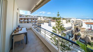 A balcony with a table and chairs, overlooking a residential area with buildings and a clear sky. - Deluxe Apartment With Balcony and Views (Rethymno)