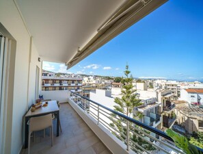 Ein Balkon mit Tisch und Stühlen, der auf ein Wohngebiet mit Gebäuden und einem wolkenlosen Himmel blickt.