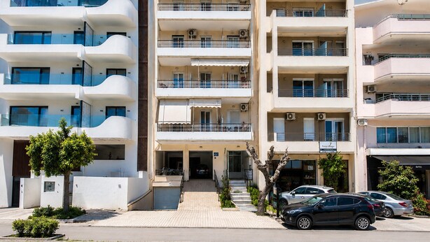 A multi-story residential building with balconies, a gated entrance, and parked cars. - Deluxe Apartment With Balcony and Views (Rethymno)
