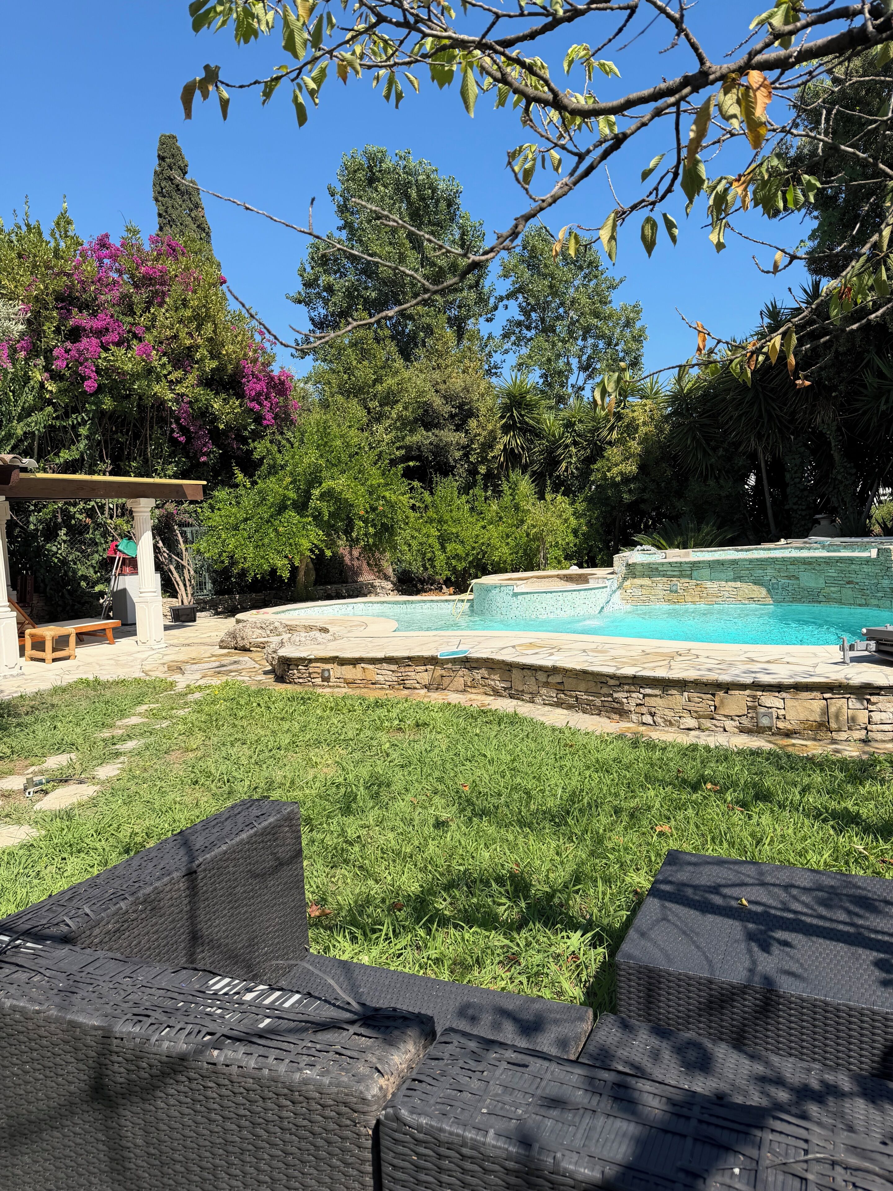 A backyard with a swimming pool, a pergola, and a grassy area with outdoor furniture.