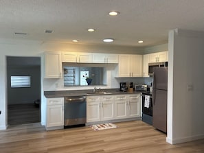A modern kitchen with white cabinets, stainless steel appliances, and recessed ceiling lights. - Sunny Cove Retreat: Walk to Beach, Dining & Marina (Deerfield Beach)