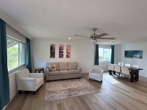 A spacious living area with a sofa, chairs, a dining table, and artwork on the walls. - Sunny Cove Retreat: Walk to Beach, Dining & Marina (Deerfield Beach)