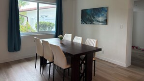 A dining area with a dark wooden table and six chairs, a window with curtains, and a painting on the wall. - Sunny Cove Retreat: Walk to Beach, Dining & Marina (Deerfield Beach)