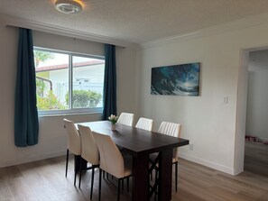 Een eetruimte met een donker houten tafel en zes stoelen, een raam met gordijnen, en een schilderij aan de muur.