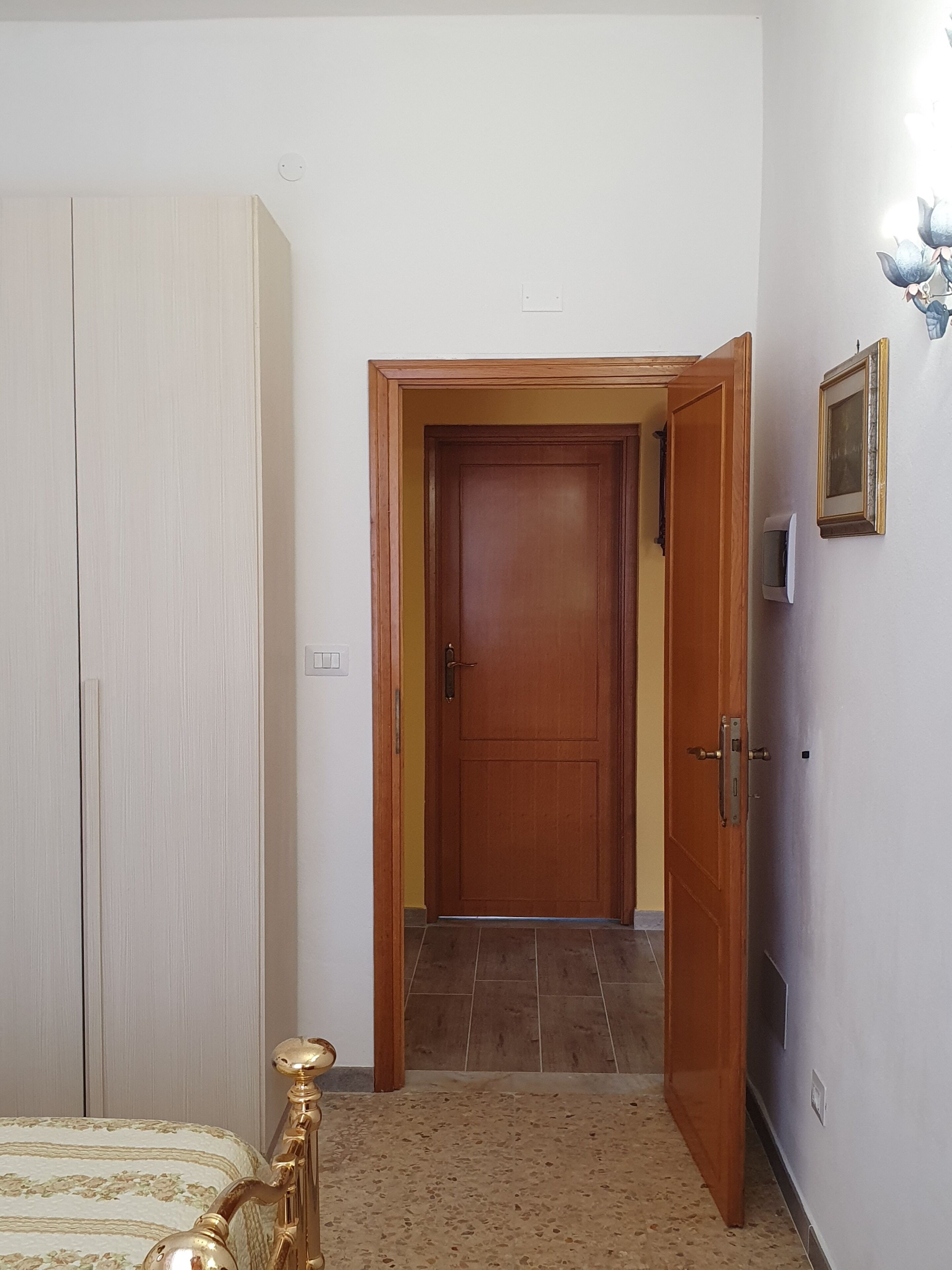 A bedroom with a bed, a wardrobe, a door leading to another room, and a wall-mounted light fixture.