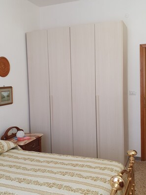 A bedroom with a bed, a wooden wardrobe, a small table with a vase, and a mirror. - The Timeless House: A Place to Visit in Tuscany (Ponsacco)