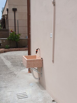 A concrete sink with a metal frame against a wall, a drainpipe, and a small plant. - The Timeless House: A Place to Visit in Tuscany (Ponsacco)