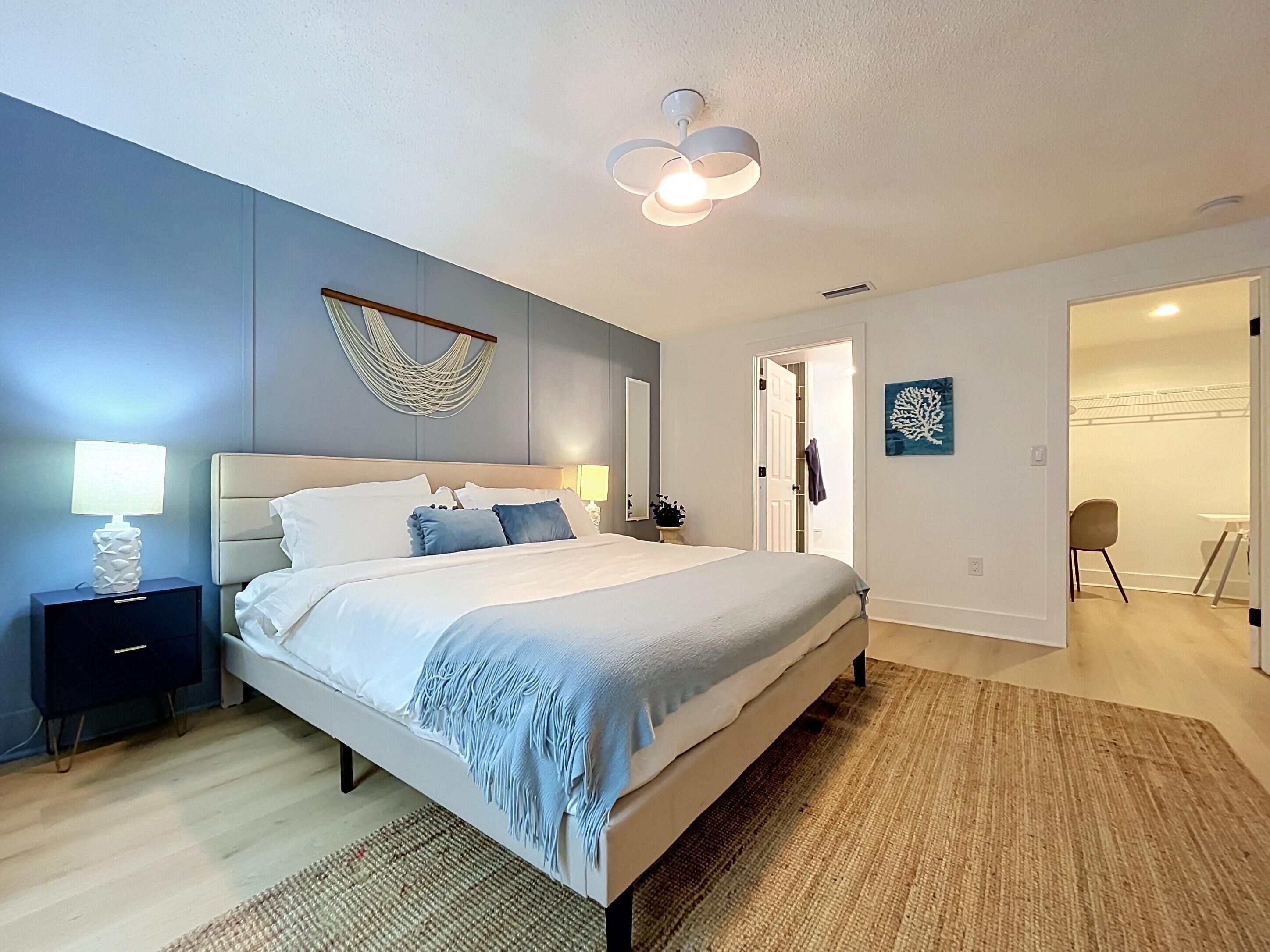 Une chambre moderne avec un grand lit, des lampes de chevet, un ventilateur de plafond et une vue sur une pièce adjacente.