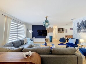A modern living room with a sectional sofa, a coffee table, and a TV mounted on the wall. - Villa Amalia/Cozy 3BR/2BA retreat.Pool/Games & Large Backyard near Anna Maria Is (Bradenton)